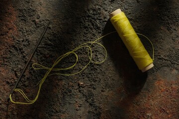 Spool of yellow thread and .needle on a dark metal background