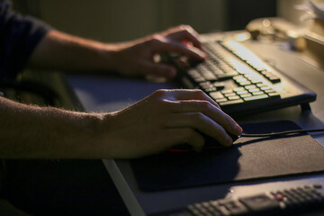 Business man working late at office at computer typing on keyboard. Male using computer for financial reports, working late overtime