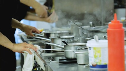 Chefs cook standing at the stove, close-up. Industrial kitchen close-up. The hands of the cooks close-up. Stainless steel cookware on the stove