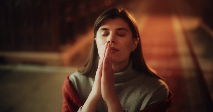 Portrait of Devout Christian Woman Siting Piously In a Church, Folding Hands For Praying, Seeking Guidance From Her Religious Faith and Spirituality. Spirit of Christianity and Belief in God