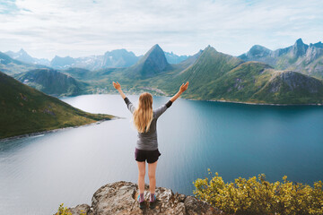 Traveler woman in Norway hiking success raised arms on the top of mountain Travel adventure active...