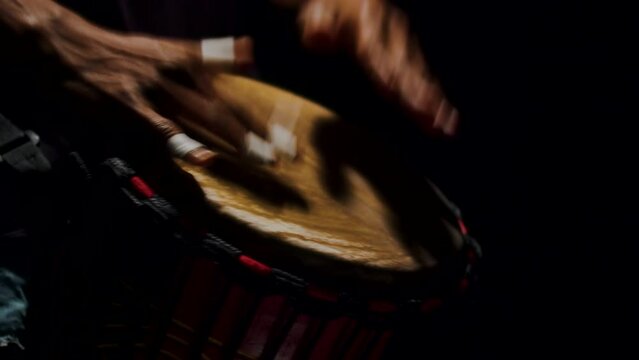 Close up of African man hands drumming on bongo in slow motion. Authentic traditional musical instrument. Musical performance in black studio