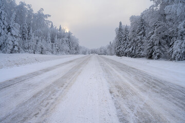 Snow and ice covered road that disappears into the distance and is surrounded by a snowy forest.
