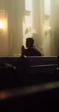 Young Christian Man Sits Piously in Majestic Church, with Folded Hands He Seeks Guidance From Faith and Spirituality while Praying. Religious Believer in the Great Power and Love of God. Slow Motion 
