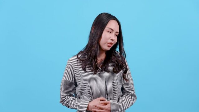 4K, Portrait Woman with long hair wearing black and white striped shirt. Asian showing stomach pain. and put his hands on his stomach and writhed around. Isolated indoor studio on blue background.