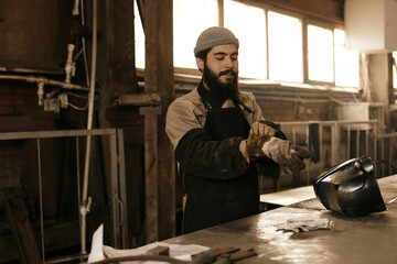 Man starting his work with putting on protective sleeves, apron and welding gloves