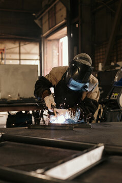 Unrecognizable welder wearing special protective helmet welding metal details using torch
