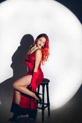 Fototapeta na wymiar Glamour lady in red dress is posing on camera in studio background