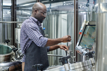 African American engineer controlling the equipment for brewing beer during his work at brewery