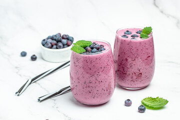 two glasses of fresh berries with yogurt smoothies fresh blueberries or bilberry on a light background. Delicious balanced food concept. top view