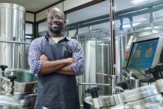 Portrait of African American engineer smiling at camera standing with his arms crossed, he working at modern brewery - Powered by Adobe