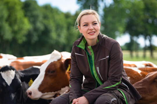 Junge Landwirtin sitzt auf einen Weidegitter, hinter ihr stehen K&uuml;he.