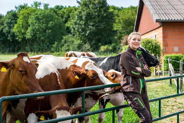  Ausbildungsberuf Landwirtschaft: Hübsche Auszubildende lehnt an einem Gatter vor einer Kuhweide. 