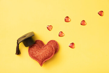 Graduated hat with two shiny hearts on a yellow background. The concept of relationship education.