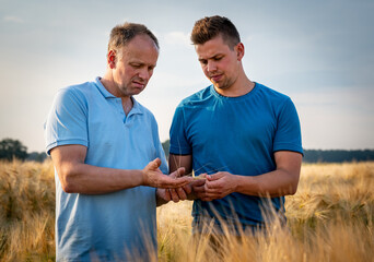 Ausbilder und sein Auszubildener stehen in einem reifen Getreidefeld, der Ausbilder zeigt an einer Pflanze, woran man die Reife des Getreides erkennen kann.