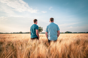 Zwei Landwirte stehen mit den Rücken zur Kamera in einem reifen Getreidefeld.