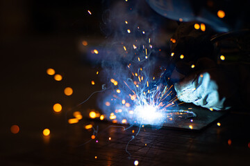 Metal welder works with a steel welder in a factory with protective equipment. Manufacture of metal structures and repair and construction services according to the concept of manual labor.