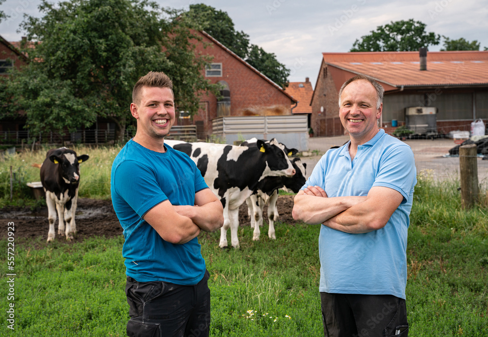 Poster landwirt mit seinem sohn auf einer wiese, im hintergrund rinder und ein hof.