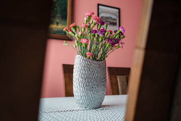 wazon z różowymi goździkami na stole - obrazy, fototapety, plakaty