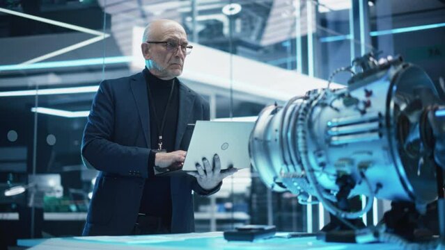 Senior Industrial Turbine Specialist Standing at a Table With an Innovative Invention. PhD Professor Using Laptop Computer to Develop a High Tech Prototype Electric Motor. 