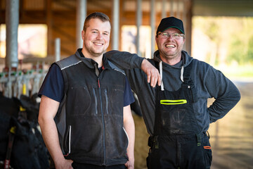Fototapeta premium Ein starkes Team: Landwirt mit seinem Hofnachfolger in einen modernen Boxenlaufstall.