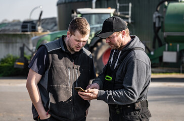  Landwirt erklärt seinen Angestellten technische Details im Hintergrund ist ein Traktor mit...