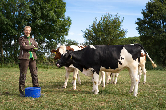 Junge Landwirtin steht in einer Rinderwiese mit Rindern.