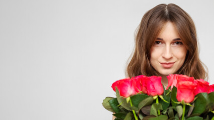 Young attractive girl with a bouquet of red roses on a white background. A happy girl with a bouquet of roses is smiling. Copy space. The concept of happiness, joy and celebration