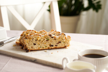Traditional german christmas pastry stollen on a marble cutting board, coffee mug, butter plate on the table cloth and scandy style kitchen chair in the back