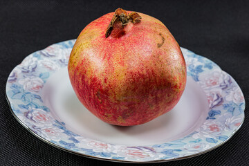 A lone pomegranate in a plate on a black background