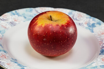 A lonely red apple on a plate on a black background