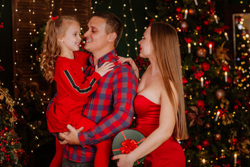 Happy family of tree with sexy mother in red clothes posing together against Christmas background. happiness and love. Focus is at the man.