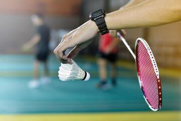 Badminton player holds racket and white cream shuttlecock in front of the net before serving it to another side of the court.