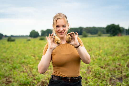 Freude über große Kartoffeln, junge landwirtschaftliche Angestellte, hält jeweils eine Kartoffel sichtbar in ihren Händen, vor einem Kartoffelfeld.
