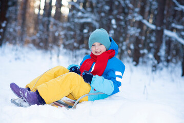 Fototapeta na wymiar happy boy downhill on a sled in winter. a child in bright clothes sits on a sled,