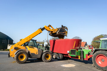 Landwirte befüllen den Futtermischwagen mit einen Hoftrac.
