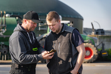 Zwei Landwirte stehen vor ihrer Biogasanlage und schauen sich die übermittelten Daten auf den...
