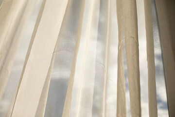 Obraz premium Transparent white curtain tulle on a sunny day, sun rays entering the room. Window curtain and fluffy clouds behind
