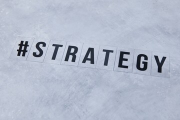 Black capital letters saying '#strategy' on concrete background. Abstract strategy slide background image. Symbol image for strategic planning. Business strategy concept image. #strategy. 
