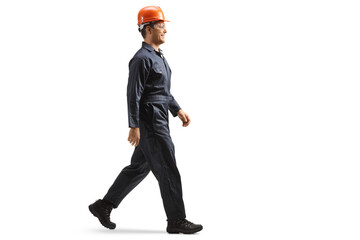Full length profile shot of a factory worker wearing a helmet and uniform and walking