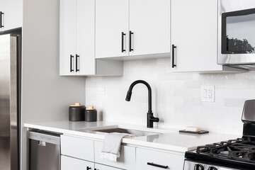 A beautiful white kitchen detail shot with a tiled backsplash, white cabinets, stainless steel appliances, and black hardware and faucet.