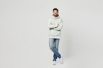 Full body smiling happy cheerful fun young man wearing mint hoody look camera hold hands crossed folded look camera isolated on plain solid white background studio portrait. People lifestyle concept.