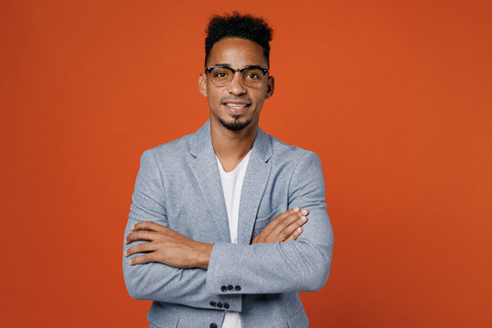 Young Confident Successful Employee Business Man Corporate Lawyer Wear Classic Formal Grey Suit Shirt Glasses Work In Office Hold Hands Crossed Folded Isolated On Plain Red Orange Background Studio.