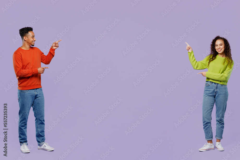 Poster Full body young couple two friends family man woman of African American ethnicity wear casual clothes together point index finger aside on area between them isolated on pastel plain purple background.