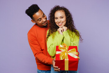 Young happy couple two friends family man woman of African American ethnicity wear casual clothes together give red present box with gift ribbon bow isolated on pastel plain light purple background.