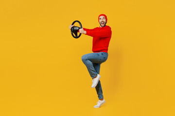 Fototapeta na wymiar Full body side profile view fun young caucasian man wear red hoody hat look camera hold steering wheel driving car isolated on plain yellow color background studio portrait. People lifestyle concept.