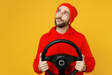 Young wistful minded dreamful pensive fun man wear red hoody hat hold steering wheel driving car look aside on area isolated on plain yellow color background studio portrait. People lifestyle concept.