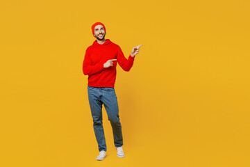 Fototapeta na wymiar Full body fun young man wear red hoody hat point index finger aside indicate on workspace area copy space mock up isolated on plain yellow color background studio portrait. People lifestyle concept.
