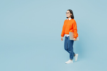 Full body side view young IT woman of Asian ethnicity wear orange sweater glasses hold closed...