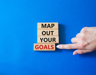 Goals symbol. Wooden blocks with words Map out your goals. Businessman hand. Beautiful blue background. Business and 'Map out your goals' concept. Copy space.